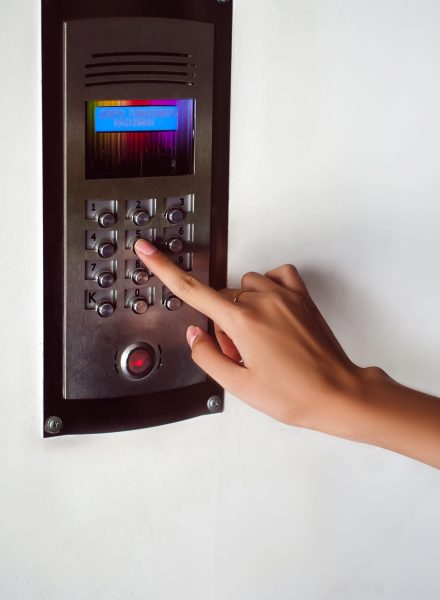 attractive woman in a blue elegant dress, dials code into intercom, at entrance of house